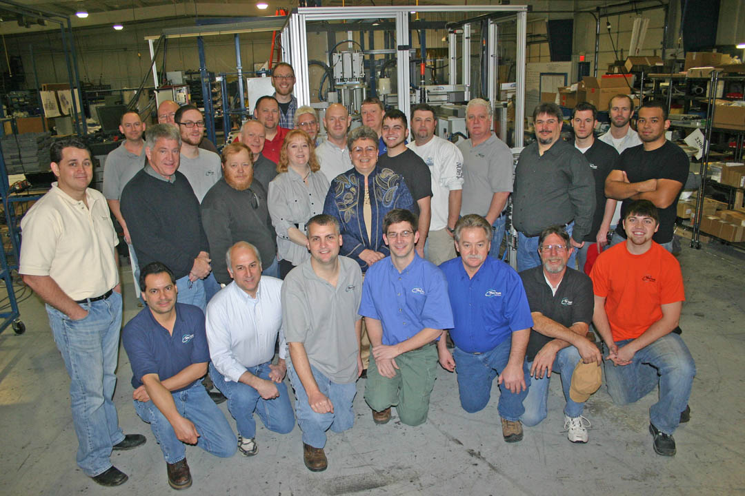 Click to enlarge,  Jerry Pedley (first standing row, second from left), founder and president of Mertek Solutions, in Sanford, and all his employees take a break from work to have their picture taken. A dozen of the employees have worked with him since he founded his first company, Electro-Mechanical Specialties, in Sanford in 1990. Pedley says his company has always had a strong partnership with Central Carolina Community College. All the employees are either graduates of or have received skill training through the college's engineering and industrial technologies programs or through its Industry Services Office. Pictured are, (kneeling, from left) Wayne Dove, Michael Moody, William McBurnett, Matt Gessner, Kevin Pedley, Chuck Nedrow, and Jacob Pedley; (first row standing, from left) Jeremy Pedley, Jerry Pedley, David Holland, Melody Hamilton, and Eve Carlyle; (second row standing, from left) Nick Newby, Tom Dupre, Clay Blanchard, Justin Pedley, Eric Carter, Mitch Poe, Jeff Spivey, and Jose Torres; and (third row standing, from left) Travis Pedley, Ronnie Holder, Kirk Pedley, Danny Swanson, Bob Pembroke, Craig Hart, Pete Ciliberto, and Blair Johnson. Not pictured are employees Chase Williams, Jesse Eckley, Robert Hamilton, James Rybolt, and Austre Gonzalez. For more information about Mertek Solutions, visit  www.merteknc.com . For more information about Central Carolina Community College's engineering and industrial technologies programs and other programs, visit  www.cccc.edu . 