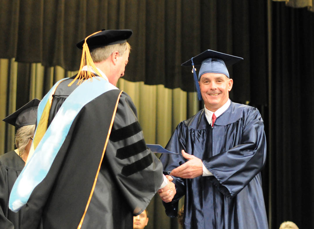 Click to enlarge,  Brian Burgess (right) of Harnett County, receives his General Educational Development diploma from Central Carolina Community College President Dr. Bud Marchant during the college's Adult High School/GED graduation Jan. 16 in the Dennis A. Wicker Civic Center. More than 400 students earned high school or GED diplomas - the largest graduating class, by far, for adult education in the college's history. About 250 graduates attended the graduation. For more information about CCCC's AHS/GED programs, visit www.cccc.edu or contact a College and Career Readiness coordinator: Chatham County, 919-545-8661 or dloges@cccc.edu; Harnett County, 910-814-8972 or mmcgee@cccc.edu; or Lee County, 919-777-7703 or esmith@cccc.edu. Para mas informacion en espanol - 919-545-8667 or jherbon@cccc.edu. 