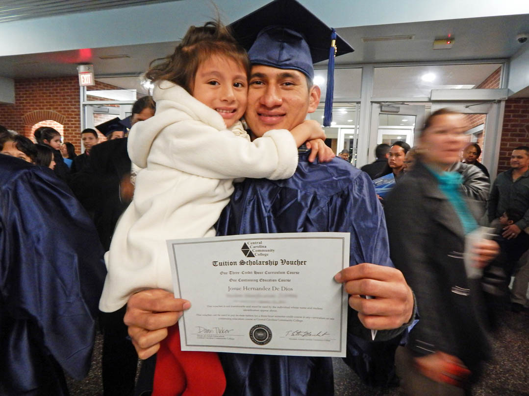 Click to enlarge,  Josue Hernandez De Dios, of Chatham County, gets a big hug from his daughter, Aura, following the Jan. 16 Central Carolina Community College Adult High School/General Educational Development graduation in the Dennis A. Wicker Civic Center. He received his GED and now plans to continue his education. He holds a CCCC Tuition Scholarship Voucher that will pay for one of his classes. More than 400 adults earned diplomas, the largest adult education class in the college's history. About 250 graduates attended the commencement. For more information about the college's AHS/GED programs, visit www.cccc.edu or contact a College and Career Readiness coordinator: Chatham County, 919-545-8661 or dloges@cccc.edu; Harnett County, 910-814-8972 or mmcgee@cccc.edu; or Lee County, 919-777-7703 or esmith@cccc.edu. Para mas informacion en espanol - 919-545-8667 or jherbon@cccc.edu. 