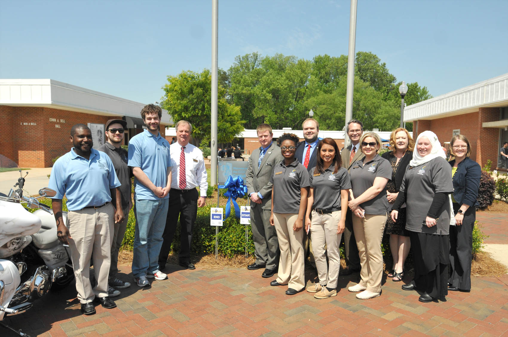 Click to enlarge,  Central Carolina Community College administrative and student leaders assembled on Wednesday, April 20, for the dedication of the new CCCC Cat Walk. The Cat Walk is a one-mile walking trail throughout the CCCC Lee County Campus. Each summer, the CCCC Student Ambassadors participate in a leadership development and team building class. The 2015-2016 Ambassadors wanted their project to benefit the entire campus community, and decided that this year's project would be to design, implement, and maintain a walking trail at the Lee Campus. Students who participate in physical education classes will be able to utilize the trail as well. The trail begins near the flagpoles, where a large map of the trail is located. The trail is a little less than a mile, and is marked by signs with the Cat Walk insignia on them that identify the  -mile and  - mile marks, trail direction, and start/end points. Each sign has a QR code that can be scanned with a smartphone, which shows a map of the trail. Student Ambassadors are Megan Blair, Cris Contreras, Christian George, Chriss Harvin, Landis Johnson, Aaron Kovasckitz, Lacey Kuenzler, Rolander Mayo, David Pope III, and Sarah Shannon-Mohamed. 