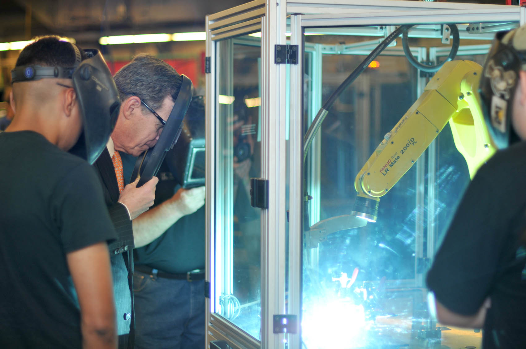 Click to enlarge,  North Carolina Gov. Roy Cooper (holding shield) gets an up-close view of a robotic welding demonstration on Wednesday, April 12, at the Central Carolina Community College Lee Main Campus. 