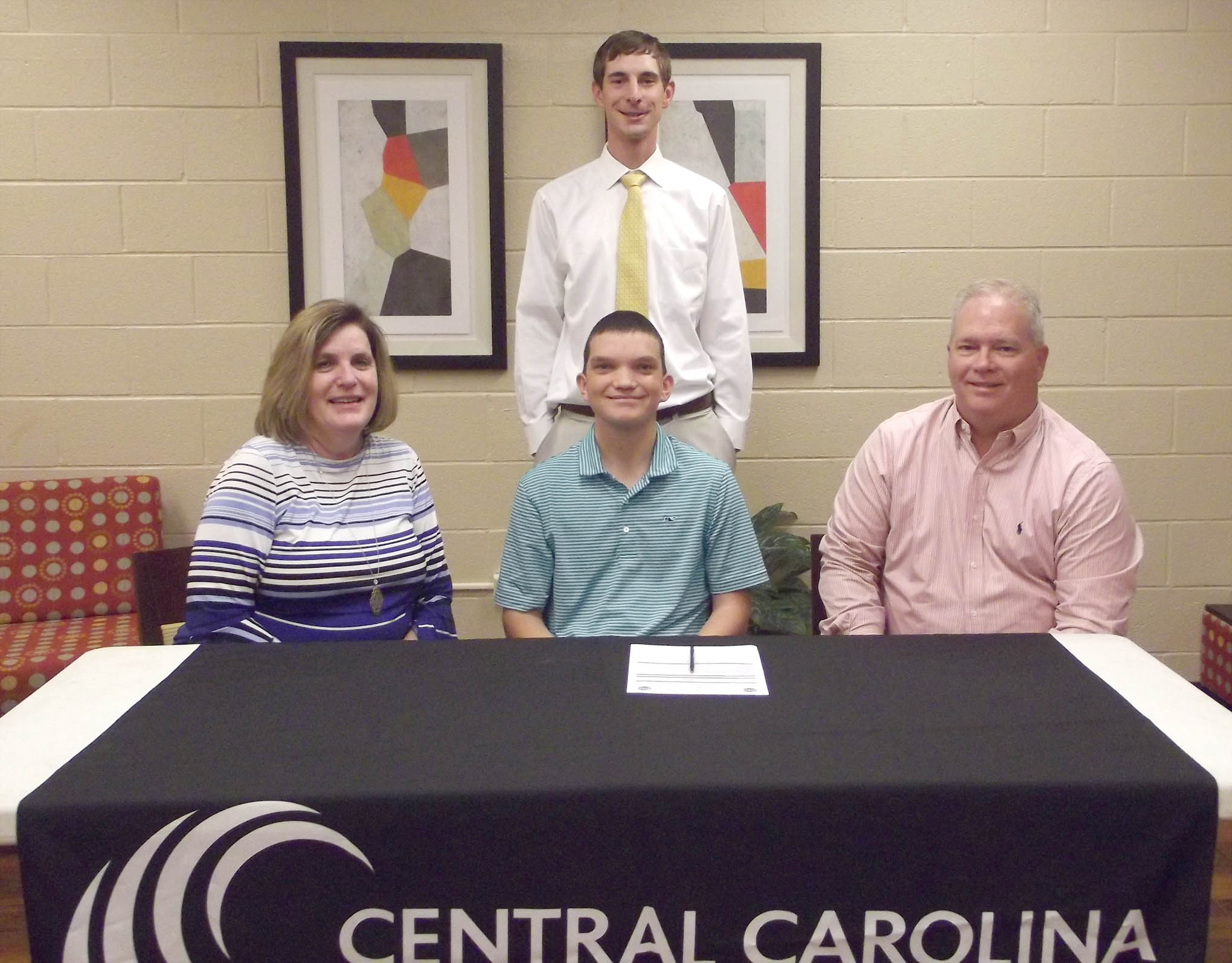 Click to enlarge,  Justin Minter (seated, center) has signed to join next year's Central Carolina Community College men's golf team. He has played golf for four years at Southern Lee High School in Sanford. "Justin is a great addition to our program," said CCCC Golf Coach Jonathan Hockaday (standing). Justin is pictured with his parents, Lisa and Ronald Minter. 