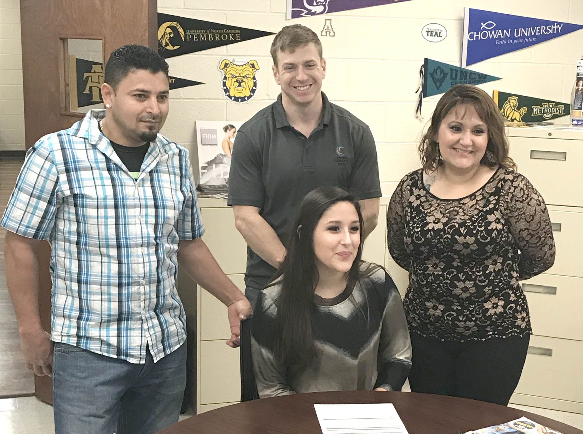 Click to enlarge,  Guadalupe Vazquez, of Sanford, signs with the Central Carolina Community College cross country program. Here, she is pictured with family members and CCCC Head Cross Country Coach Jacob Ashworth. 