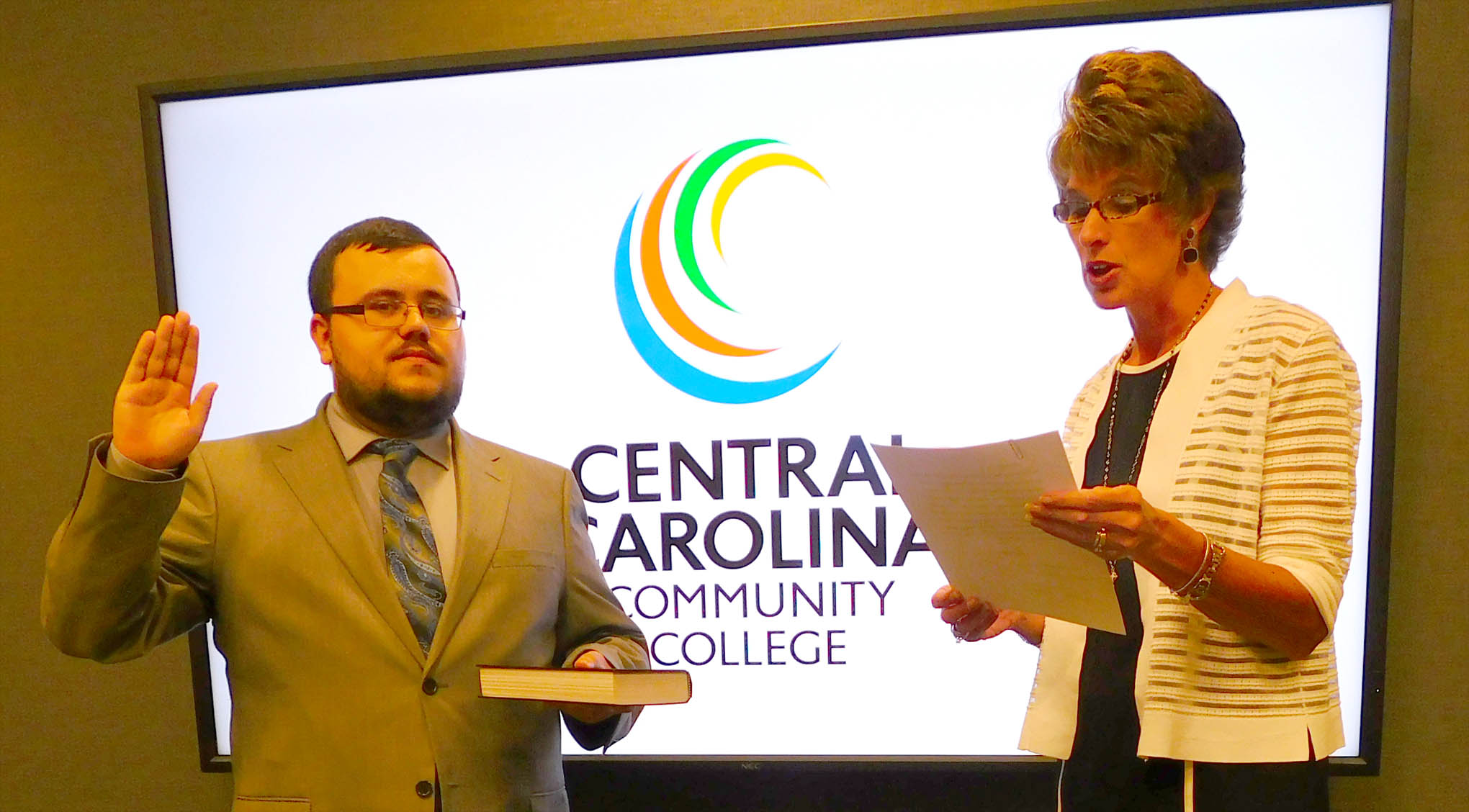 Click to enlarge,  Central Carolina Community College Student Government Association President Dylan Hargis, of McGee's Crossroads, is sworn in as an ex-officio member of the CCCC Board of Trustees' meeting on Wednesday, July 25. Susie K. Thomas (right), Clerk of Superior Court in Lee County, conducted the ceremony. 