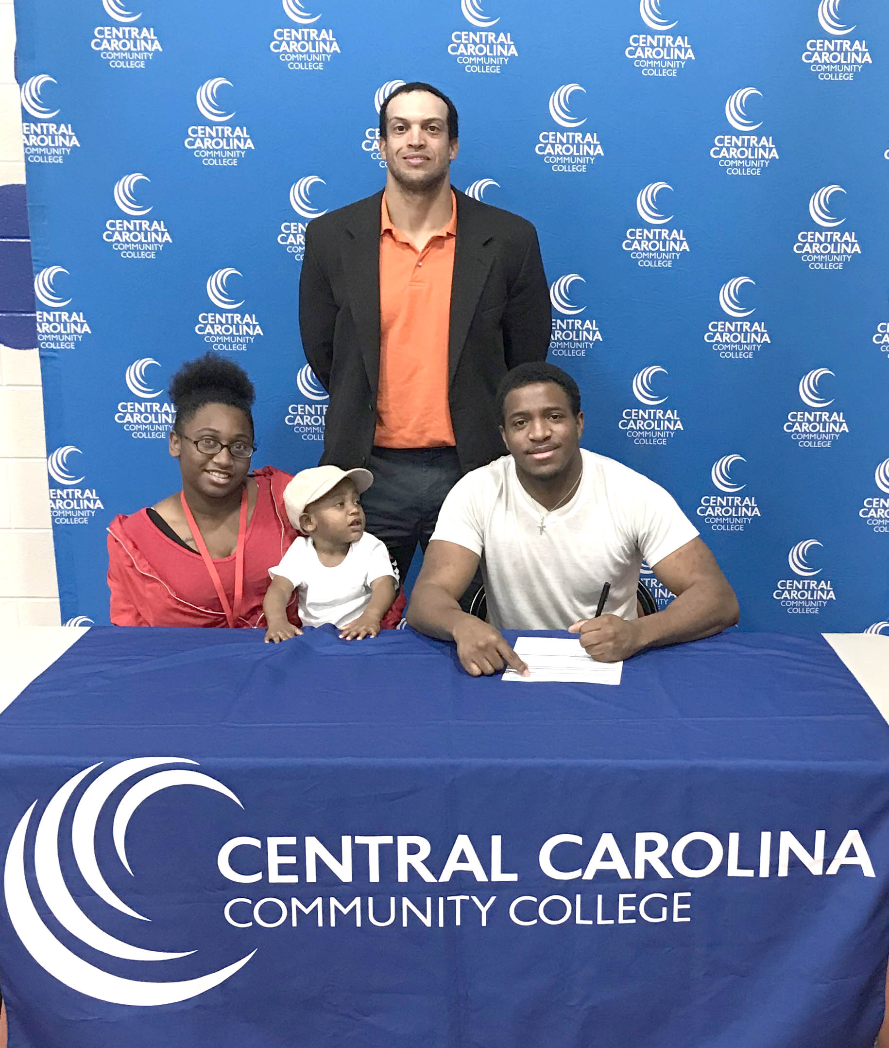 Click to enlarge,  Tyree Minor (seated, right) signs with the Central Carolina Community College cross country program as his sister, Destiny Minor, and nephew, Jace Minor, join him at the signing. Standing is CCCC Head Cross Country Coach Richard Briggs. 