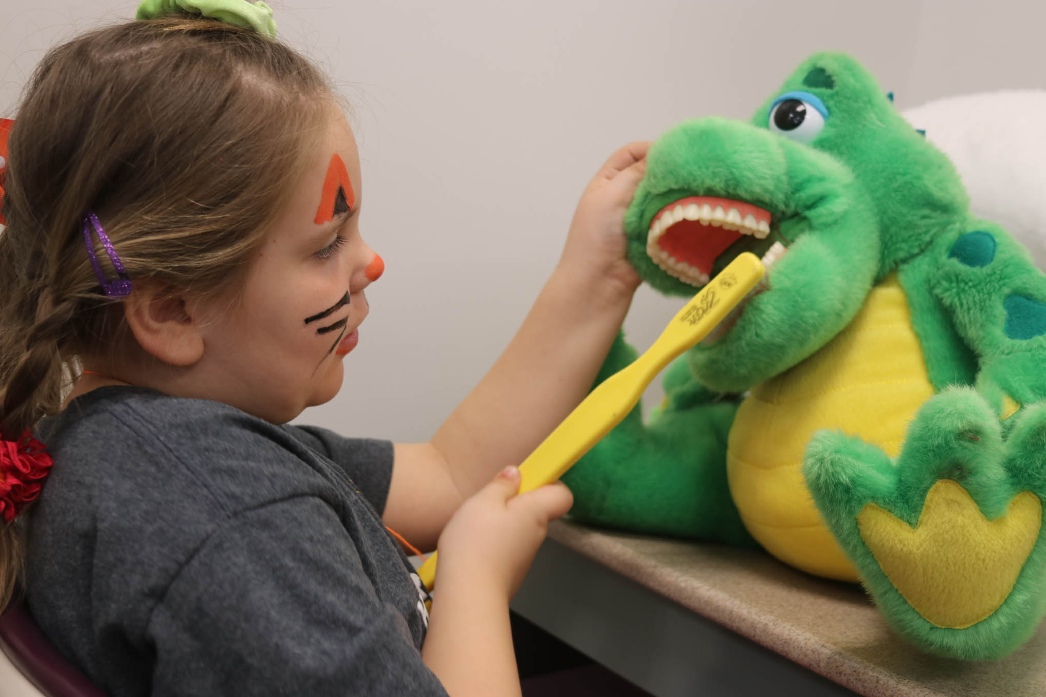 Click to enlarge,  A student learns how to brush teeth using an oversized toothbrush and stuffed animal during Give Kids A Smile Day at Central Carolina Community College. 