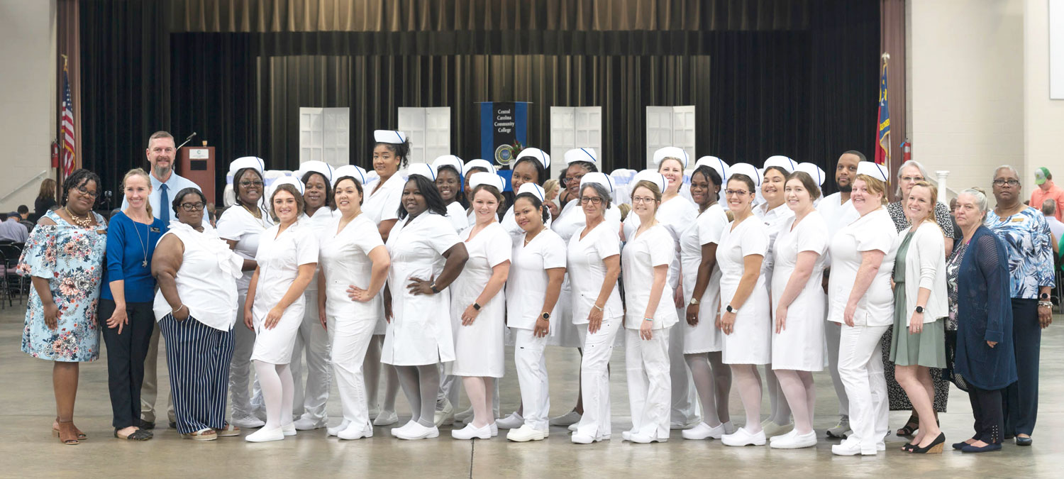 Click to enlarge,  The Central Carolina Community College Louise L. Tuller School of Nursing Practical Nursing held its pinning and candle lighting ceremony on Thursday, July 21, at the Dennis A. Wicker Civic &amp; Conference Center in Sanford. Class members - with home towns listed - and faculty members are pictured, left to right: front row, Practical Nursing Lead Instructor Christie McDougald, Adjunct Sarah TenBrink, Instructor Crystal Bennett, Giovanna Conigliaro (Raleigh), Trisha Scott (Fayetteville), Tamika McDougal (Sanford), Amy Kautz (Cameron), Vaniza Bailey (Cameron), Robin Beach (Sanford), Megan Bodily (Sanford), Natasha Campbell (Raleigh), Bianca Raby (Raleigh), Julia Hodges (Dunn), Beverly Autrey (Sanford), Adjunct Emily Long, and Instructor Theresa Cebulski-Field; back row, Instructor Chris Bailey, Monique Peguese (Wadesboro), Camia Woods (Siler City), Carmen Monroe (Carthage), Stella Jayala (Durham), Taylor Woodard (Raleigh), Ceria Hollingsworth (Parkton), Erica Carvin (Fayetteville), Rebecca Casanova (Fuquay-Varina), Jazmine Pritchett (Fort Bragg), Melvin Littlejohn (Bunnlevel), Department Chair Dr. Barbara Campbell, and Instructor Juanita Carter. For more information on the CCCC Practical Nursing program, visit www.cccc.edu/curriculum/majors/nursing/Nursing-Department/. 
