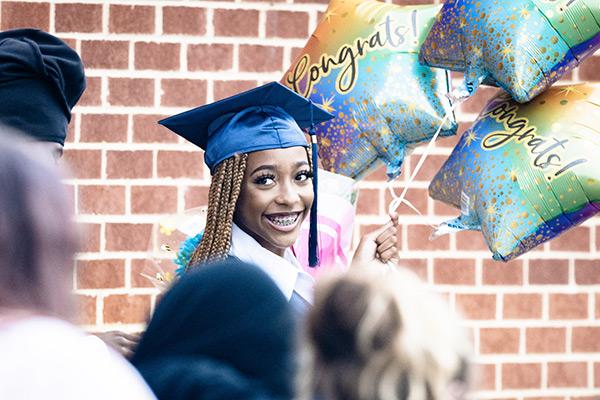 Adult High School graduate at graduation holding balloons 