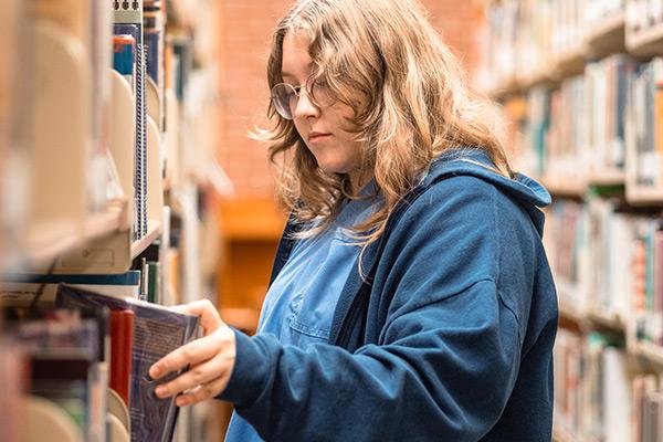 Student pulling book from library shelf