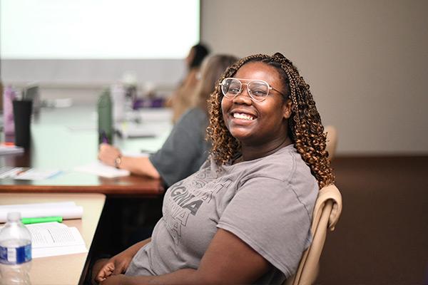 Adult student leaning back from her desk smiling at the computer 