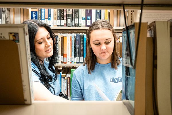 Two students looking through books in the library 