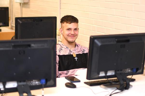 Student smiling, sitting between computers 